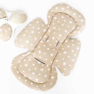 Op de afbeelding: Een beige baby autostoeltje inzet met een wit sterrenpatroon. De inzet is ontworpen om extra ondersteuning en comfort te bieden voor een baby in een autostoeltje.