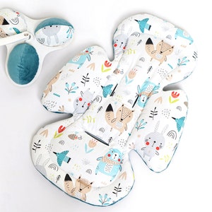 Op de afbeelding: Een witte babyzitting-inleg met een blauwe rand en een fantasierijke print met bosdieren, waaronder vossen, konijnen, vogels en beren. De inleg is ontworpen om baby's in autostoeltjes, kinderwagens en wipstoeltjes ondersteuning en comfort te bieden.