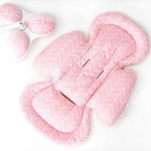 Op de afbeelding: Roze baby autostoeltje inzet met een wit chevron patroon. De inzet heeft een hoofdsteun en een lichaamsondersteuning.
