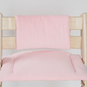 Op de afbeelding: Een roze gepolsterde zitting en rugleuning voor een kinderstoel. De stoel is gemaakt van natuurlijk hout.