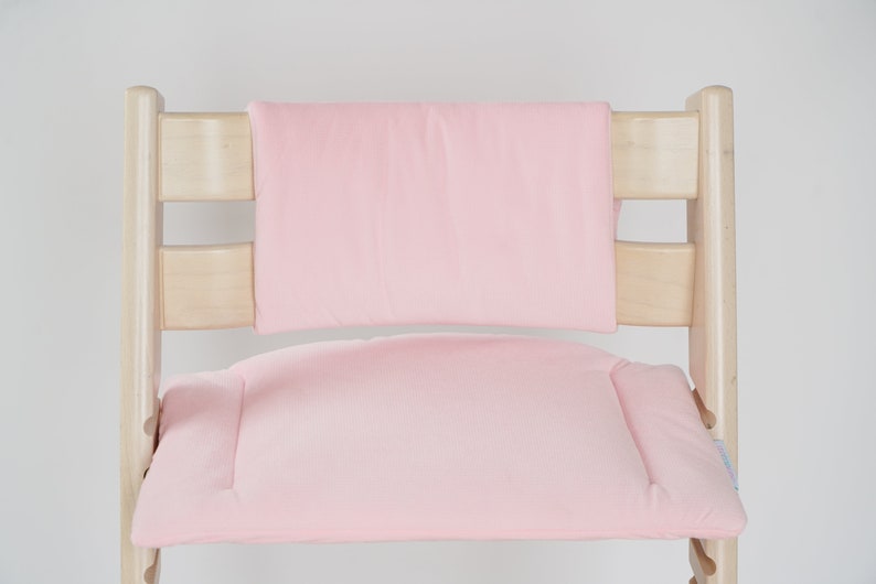 Op de afbeelding: Een roze gepolsterde zitting en rugleuning voor een kinderstoel. De stoel is gemaakt van natuurlijk hout.