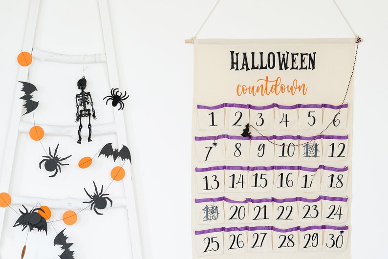 May include: A Halloween countdown calendar with 30 numbered pockets, purple trim, and a hanging bat and spider decoration. A garland with orange circles, bats, and spiders hangs on a white ladder.