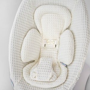 以下が含まれることがあります： クリーム色のベビーシートインサート、ワッフル織りのテクスチャ。 インサートは、ヘッドレスト、サイドサポート、座席エリアを備え、すべて同じテクスチャ生地で作られています。 白いプラスチック製のバックルが見えます。 全体的なデザインは柔らかく、クッション性があります。