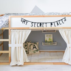 Puede incluir: Una litera de madera con una cabecera blanca y un dosel de tela blanca. La cabecera tiene una pancarta negra que dice "My Secret Place". La cama tiene un edred&oacute;n a cuadros blanco y negro y una almohada blanca.