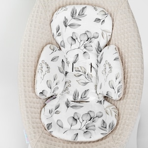 Op de afbeelding: Een witte en grijze baby-schommelstoel-inzet met een bloemenpatroon. De inzet is gemaakt van zachte stof en heeft een comfortabel ontwerp.