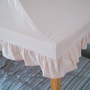 May include: A light pink fabric canopy cover featuring a ruffled edge trim. The canopy is designed to fit over a wooden frame structure, providing a soft, solid-colored textile top with gathered fabric detailing along the perimeter of the frame.