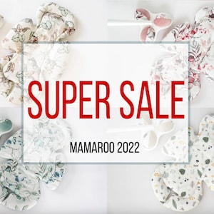 May include: Four different patterned baby seat inserts for a MamaRoo swing. The inserts are in various floral patterns with green, white, and pink colours. The text "SUPER SALE" is in red letters and the text "MAMAROO 2022" is in black letters.