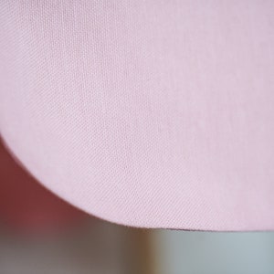 K&ouml;nnte beinhalten: Nahaufnahme eines blassrosa Stoffes mit einer dezenten gewebten Textur. Der Stoff ist glatt und weich, mit einer leicht abgerundeten Kante.