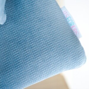 May include: Close-up of a blue fabric with a textured weave. A white tag with the text "ITS FOR KIDS" is attached to the fabric. The fabric is a solid light blue color.