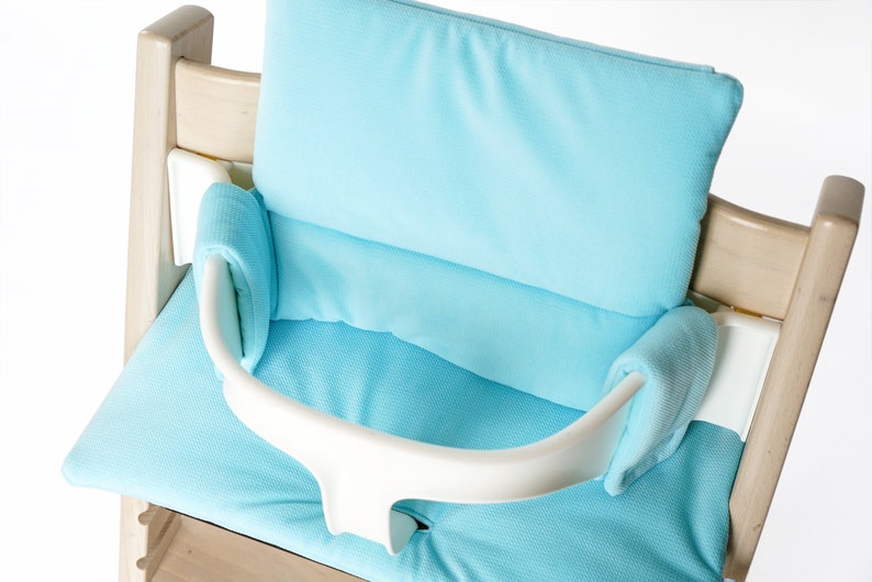 Pu&ograve; includere: Un seggiolone imbottito di colore azzurro chiaro con una cintura di sicurezza bianca.