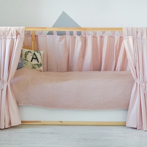 May include: A wooden bed frame with pink curtains and a pink and white checkered blanket. The bed is styled with a pillow with a green leaf and the letter A on it.