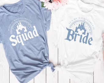 May include: Two white t-shirts with a blue graphic of Cinderella's castle and Mickey Mouse ears. One shirt says "It's My Bachelorette Bride" and the other says "Magical Bachelorette Squad".