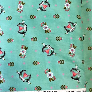 May include: A fabric bolt featuring a repeating pattern of floral and wreath designs in pink, white, and green on a teal background. The fabric includes the text "Slow & Steady by TULA PINK. PWTP 089 Winner's Circle."