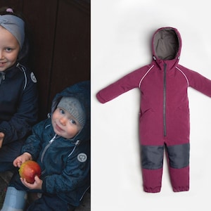 Peut inclure: Deux enfants portant des vestes d'hiver bleues et tenant des pommes rouges. L'enfant de gauche porte un bandeau gris. L'enfant de droite porte un chapeau gris. L'arrière-plan est une porte en bois.