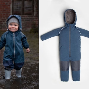 Peut inclure: Une combinaison de neige imperméable bleue avec une capuche et des bordures blanches. La combinaison a une fermeture éclair et un panneau gris contrastant sur les jambes.