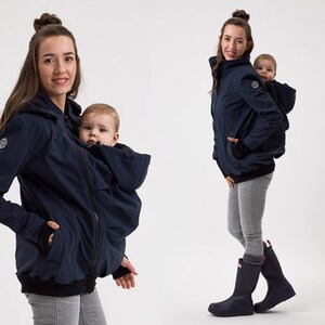 May include: A navy blue jacket with a built-in baby carrier. The jacket has a hood and a zip closure. The carrier has a zipped opening at the front and a hood for the baby. The jacket is being worn by a woman and a baby is in the carrier.