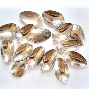 May include: A collection of 12 silver spoons, each with a unique shape and design. The spoons are arranged in a random pattern on a white surface.