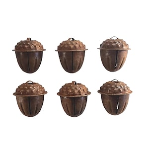 May include: Six antique metal acorn ornaments with textured caps and vertical slit details. The ornaments have a rustic, aged appearance, with a warm brown color. Each acorn has a small loop at the top for hanging, suggesting they are intended for seasonal decor.