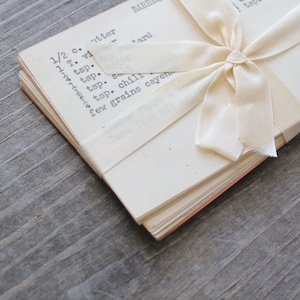 May include: A pack of 10 vintage recipe cards tied with an off-white ribbon.   The overall style evokes nostalgia and a sense of home cooking.