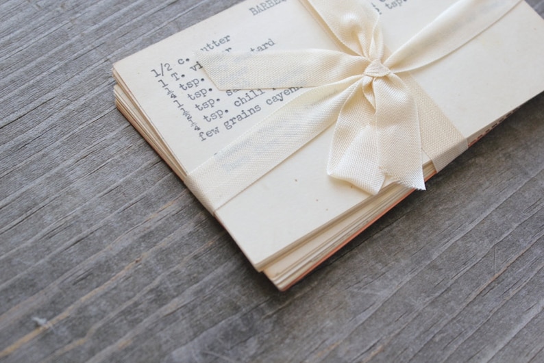 May include: A pack of 10 vintage recipe cards tied with an off-white ribbon.   The overall style evokes nostalgia and a sense of home cooking.