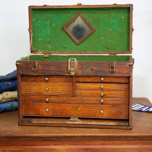 May include: An antique wooden tool chest with multiple drawers and a hinged lid. The interior is lined with green felt and features a small mirror. The chest is made of dark wood and has brass hardware.