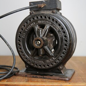 May include: A black cast iron electric motor with a cord and plug. The motor has a round shape with a central hub and spokes. The text "The Paragon Electric Mfg. Co. St. Louis, U.S.A." is inscribed on the motor.