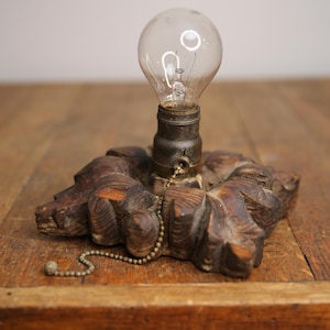 May include: A vintage wooden lamp base with a pull chain and a clear light bulb. The base is intricately carved with a floral design.