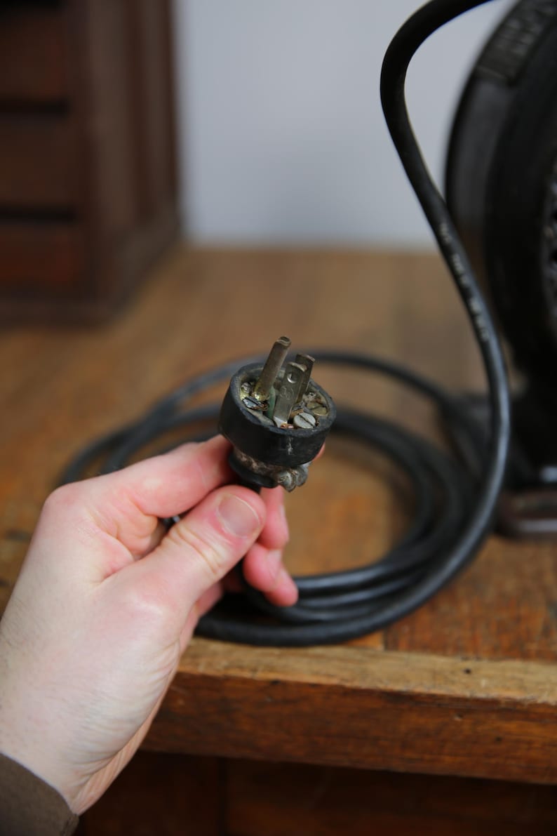 May include: Close-up of a black electrical cord with a two-prong plug. The plug is connected to a vintage electrical device.