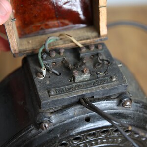May include: Close-up of an antique electric motor with exposed wiring and a wooden box. The motor has a black metal casing with a label that reads "Dickens Automatic Switch".