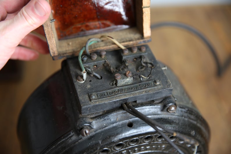 May include: Close-up of an antique electric motor with exposed wiring and a wooden box. The motor has a black metal casing with a label that reads "Dickens Automatic Switch".