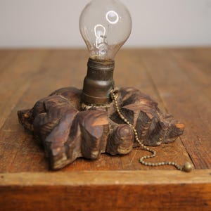Puede incluir: Una base de l&aacute;mpara de madera con un dise&ntilde;o tallado y una bombilla adjunta. La l&aacute;mpara tiene una cadena de tracci&oacute;n para encender y apagar la luz.