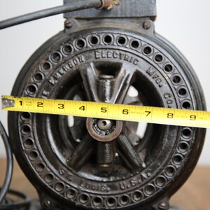 May include: A black cast iron Emerson Electric Mfg. Co. motor with a 11-inch diameter. The motor has a circular, black, metal casing with a series of holes around the edge. The motor is labeled "Emerson Electric Mfg. Co. St. Louis, U.S.A."