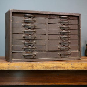 May include: A vintage wooden cabinet with two columns of drawers. Each drawer has a curved metal handle. The cabinet is a dark brown color and sits on a wooden table. The cabinet is likely used for storage.