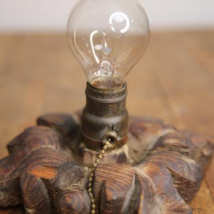 Puede incluir: Una base de l&aacute;mpara de madera con un dise&ntilde;o decorativo tallado. Una bombilla est&aacute; unida a la base con un interruptor de cadena.