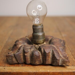 Puede incluir: Una bombilla vintage con una base de madera. La bombilla es de vidrio transparente y tiene un filamento met&aacute;lico. La base es de madera tallada y tiene un acabado marr&oacute;n oscuro.