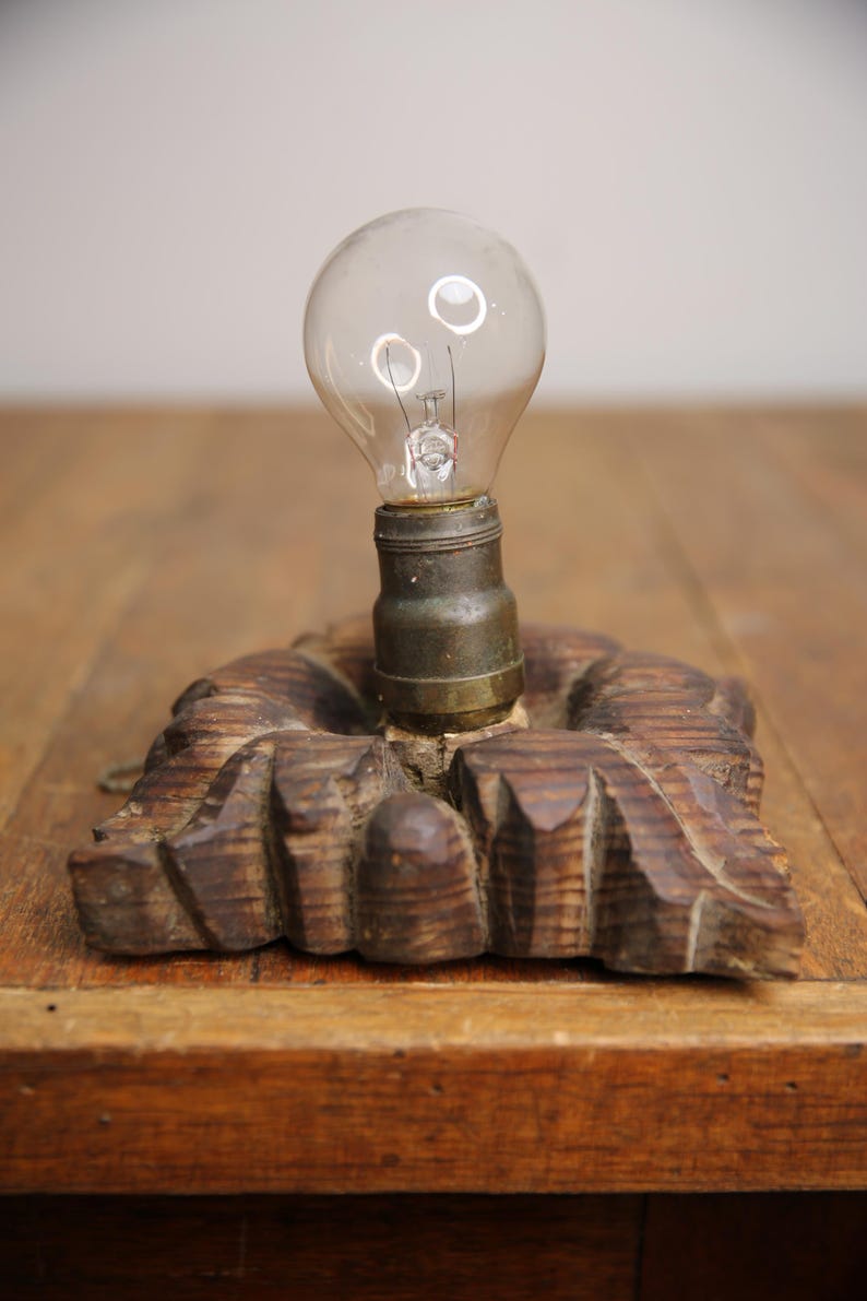 Puede incluir: Una bombilla vintage con una base de madera. La bombilla es de vidrio transparente y tiene un filamento met&aacute;lico. La base es de madera tallada y tiene un acabado marr&oacute;n oscuro.