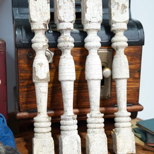 May include: Four vertical wooden balusters featuring a distressed white painted finish with visible cracks and peeling paint. Each baluster has a square base, a series of rounded decorative rings in the center, and a square top section.