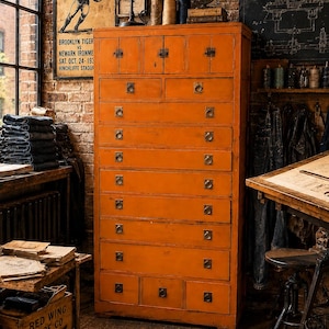 May include: An orange wooden cabinet with multiple drawers and metal ring pulls. A vintage football poster hangs above the cabinet. The room has a rustic, industrial aesthetic with exposed brick and vintage decor.