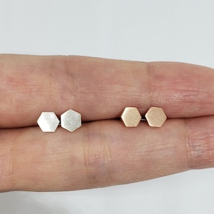 May include: Two pairs of hexagon-shaped stud earrings. One pair is silver and the other is rose gold.