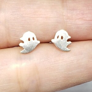 May include: A pair of silver ghost stud earrings. The earrings are small and delicate, and they feature a simple ghost design.