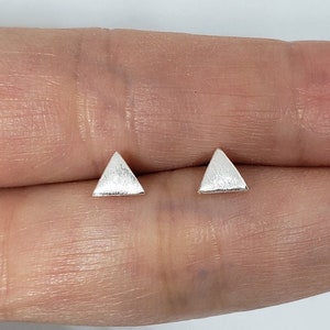 May include: A pair of silver triangle stud earrings. The earrings are small and have a brushed finish.