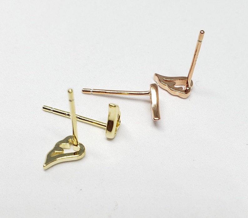 May include: A pair of gold heart-shaped earrings with a post back closure. The earrings are on a white surface.