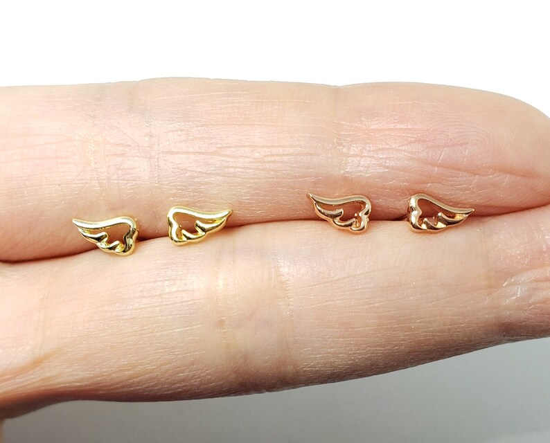 May include: A pair of gold and rose gold angel wing earrings. The earrings are small and delicate, and they are perfect for everyday wear.