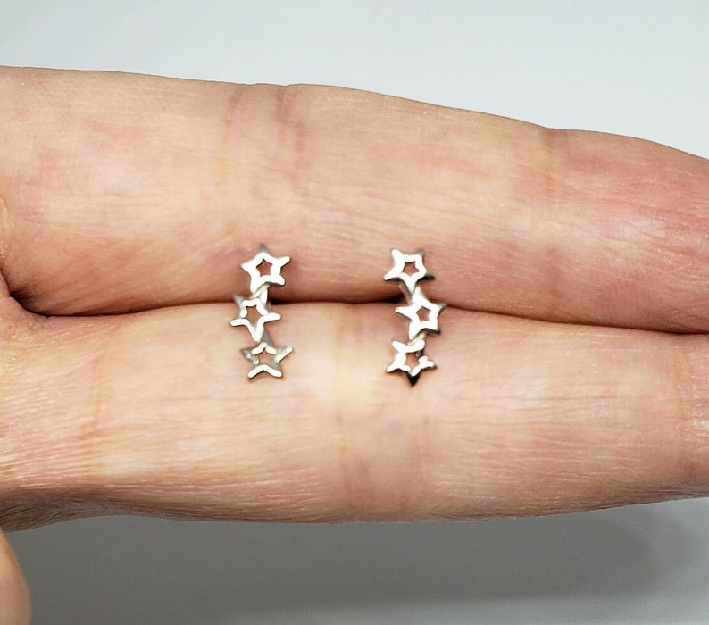 May include: A pair of silver star-shaped earrings. Each earring features five connected stars in a row.
