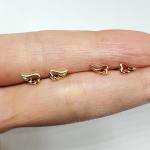 May include: A pair of gold and rose gold angel wing earrings. The earrings are small and delicate, and they are perfect for everyday wear.
