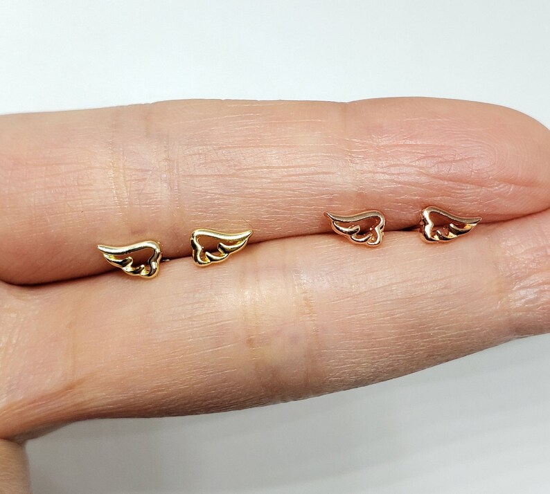 May include: A pair of gold and rose gold angel wing earrings. The earrings are small and delicate, and they are perfect for everyday wear.