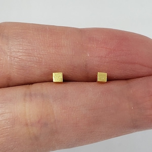 May include: A pair of gold square stud earrings. The earrings are small and have a brushed finish.