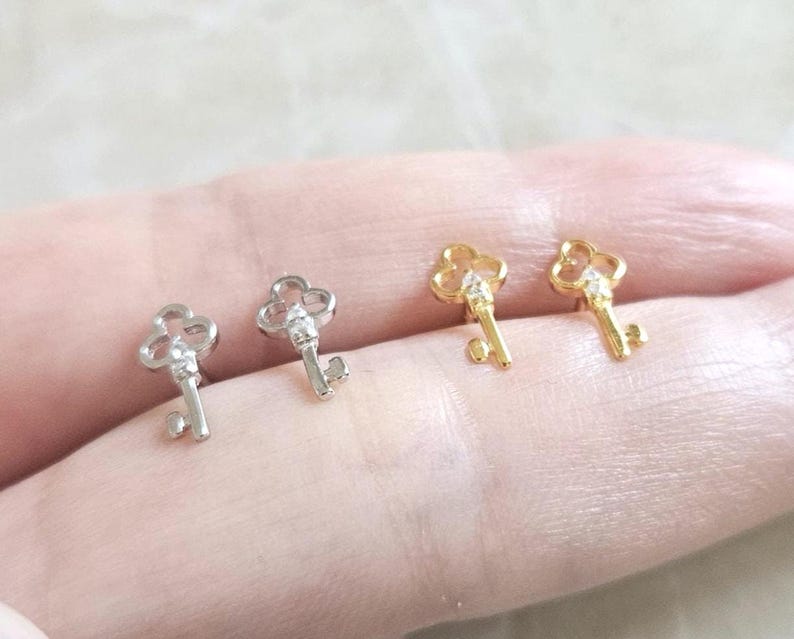 Puede incluir: Cuatro pendientes con forma de llave. Dos son plateados y dos dorados. Cada llave tiene una parte superior decorativa y una peque&ntilde;a gema transparente. Los pendientes son peque&ntilde;os y delicados.