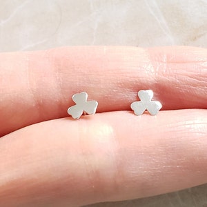 May include: A pair of silver clover-shaped stud earrings. The earrings are small and delicate, and they are perfect for everyday wear.