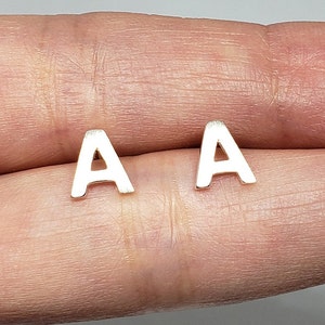 May include: A pair of silver letter A earrings. The earrings are small and delicate, and they are perfect for everyday wear.